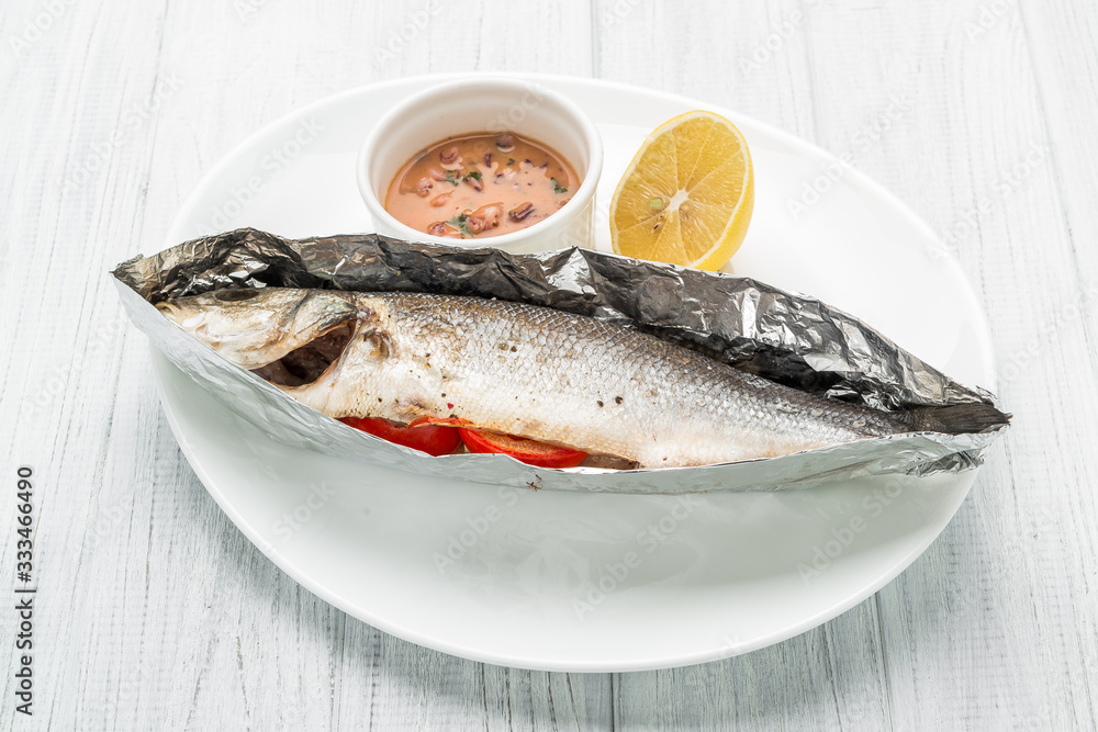 Baked sea bass with vegetables close up shoot on wooden background Baked sea bass with vegetables close up shoot on wooden background