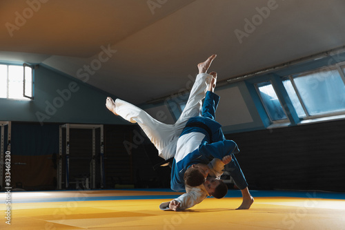 Fototapeta Two young judo caucasian fighters in white and blue kimono with black belts training martial arts in the gym with expression, in action, motion. Practicing fighting skills. Overcoming, reaching target