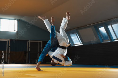 Two young judo caucasian fighters in white and blue kimono with black belts training martial arts in the gym with expression, in action, motion. Practicing fighting skills. Overcoming, reaching target photo