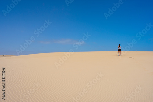 Beautiful Young tanned  brunette  woman   walking on sand dunes or desert against blue sky. Corralejo  Fuerteventura  Canary Islands  Spain 