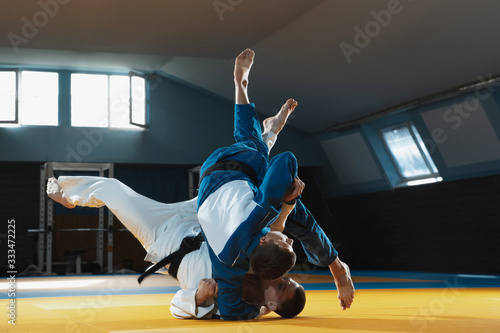 Two young judo caucasian fighters in white and blue kimono with black belts training martial arts in the gym with expression, in action, motion. Practicing fighting skills. Overcoming, reaching target photo