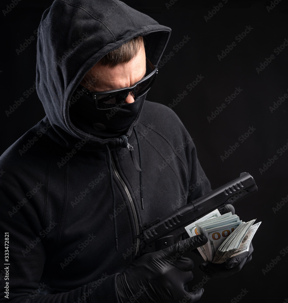 Man in black mask and hoody with a gun and pack of dollars Man in black mask and hoody with a gun and pack of dollars