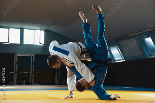 Two young judo caucasian fighters in white and blue kimono with black belts training martial arts in the gym with expression, in action, motion. Practicing fighting skills. Overcoming, reaching target photo