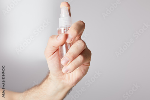 cropped view of man holding hand sanitizer in spray bottle on grey background