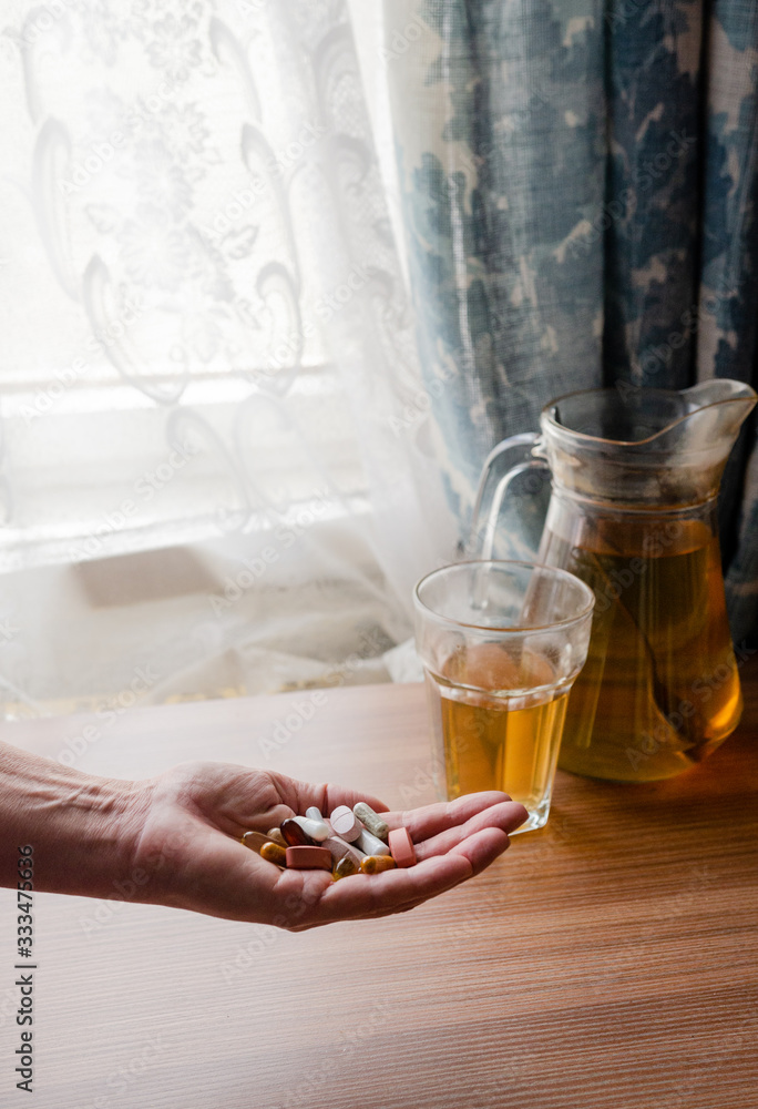 Woman holds pills in her hand - in the background herbal tee - vitamins - dietary supplements - immune system boost Woman holds pills in her hand - in the background herbal tee - vitamins - dietary supplements - immune system boost