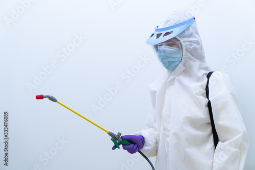 worker in personal protective equipment including white suit mask and face shield sparaying disinfectant to control coronavirus infection (focus at hand)