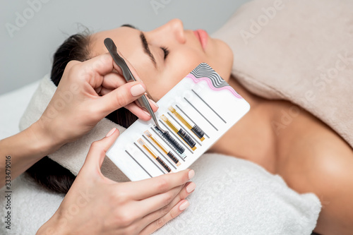 Beautician takes eyelashes by tweezers.