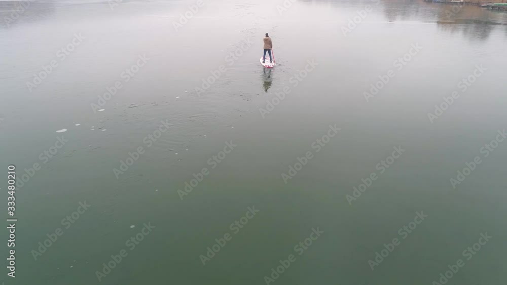Man standing on stand up paddleboard on icy lake Man standing on stand up paddleboard on icy lake