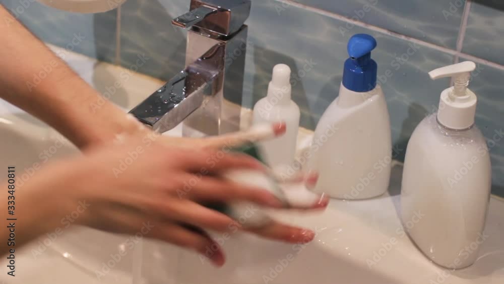woman washing her hands using blue sponge in blue and white bathroom interior with white soap and sanitizer bottles on a sink woman washing her hands using blue sponge in blue and white bathroom interior with white soap and sanitizer bottles on a sink