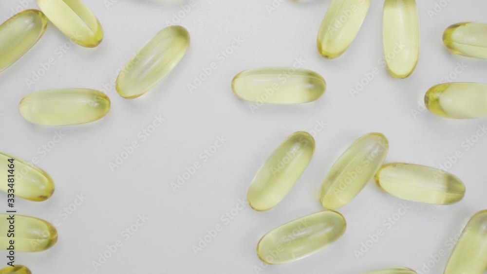 Vitamin E or fish oil yellow capsules falling on white surface. Slow motion. Vitamin E or fish oil yellow capsules falling on white surface. Slow motion.