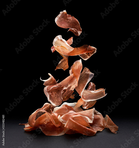 Falling jamon slices, raw pork ham isolated on black background