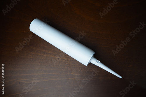 Sealant cartridge on the table. White caulk on wood table. Sealant for fix water leak.