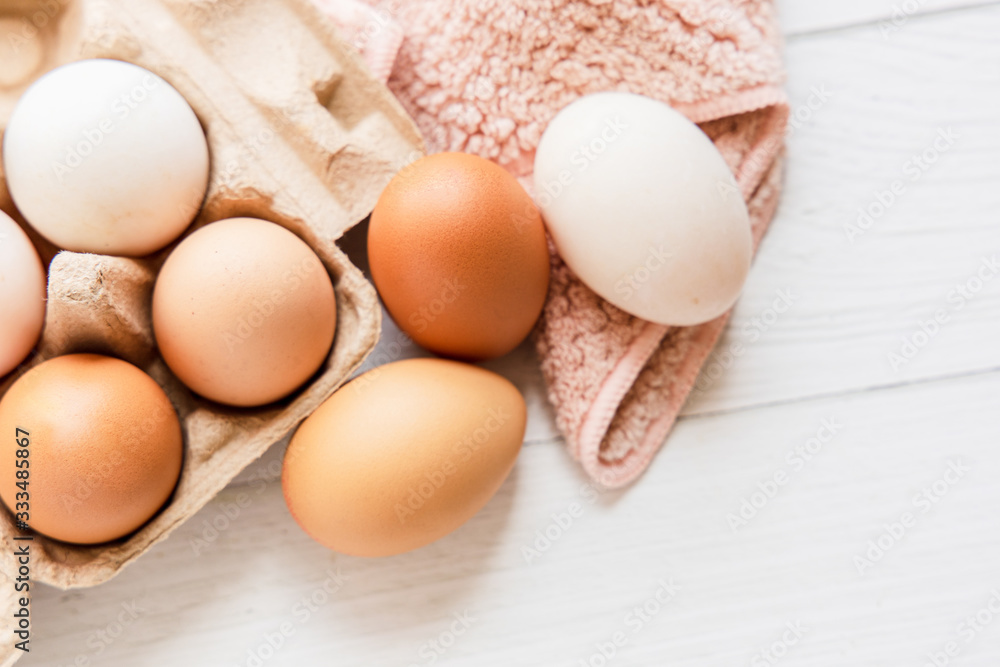 Brown and white organic chicken eggs in a brown paper box placed on a white wooden table. Eggs provide protein, suitable for health lovers. Brown and white organic chicken eggs in a brown paper box placed on a white wooden table. Eggs provide protein, suitable for health lovers.