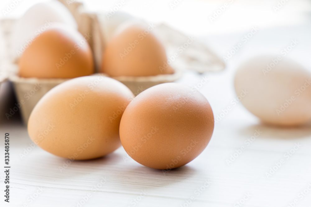 Brown and white organic chicken eggs in a brown paper box placed on a white wooden table. Eggs provide protein, suitable for health lovers. Brown and white organic chicken eggs in a brown paper box placed on a white wooden table. Eggs provide protein, suitable for health lovers.