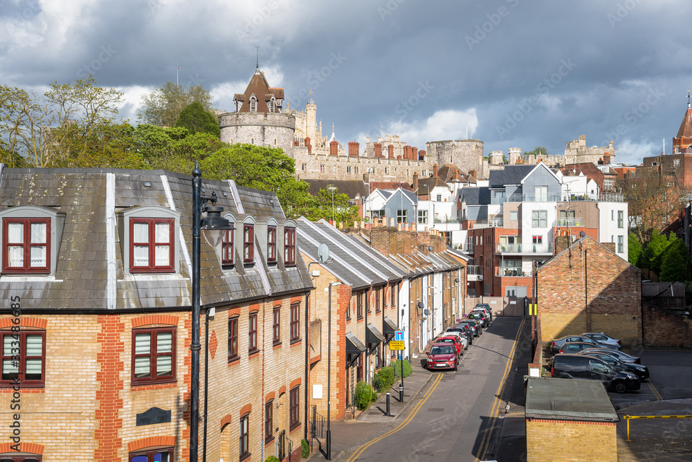 View of a street lined with traditional terraced houses in a town centre under stormy clouds on a spring day. Some modern aparment buildings are visible in background.