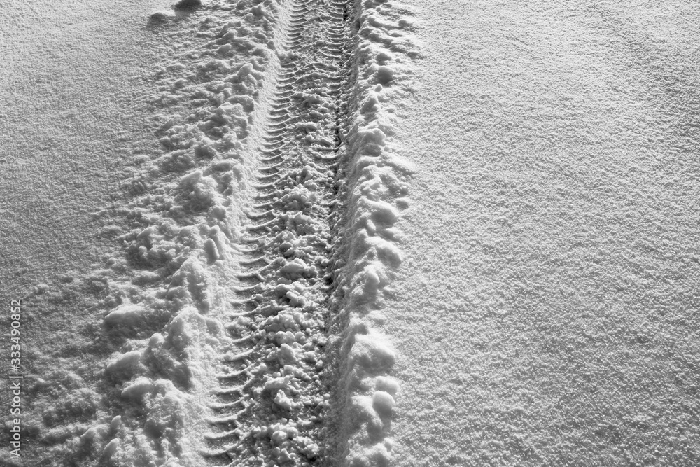 The footprint of a car wheel in the snow. The road in the winter time.