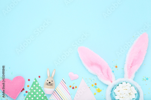 Easter concept. Rabbit ears with paper flags, fabric heart and marshmallows on blue background