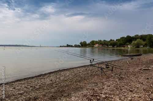 Musov Lake - two fishing rods on the shore of a lake bay with dramatic sky in the background a fishing boat