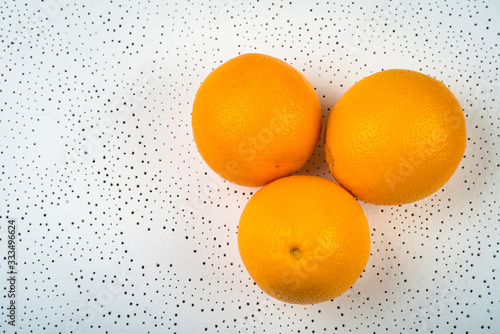 three whole oranges are dotted on a white surface