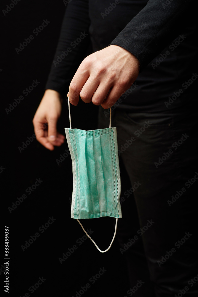 A man in black clothes on a black background holds a protective mask in his hand. A man in black clothes on a black background holds a protective mask in his hand.