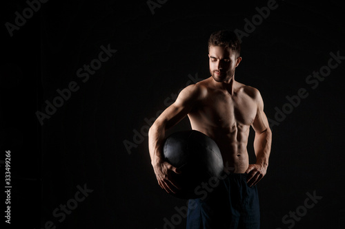 a male athlete in good physical shape on a black background with a medball in his hands