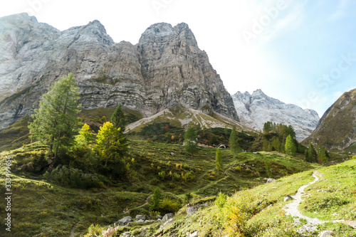 A change of the seasons in Carnic Alps, Austrian-Italian border. There is path way across the valley. Sun rays coming from above the peaks. Lower parts are green, turning yellowish. Peace of mind.