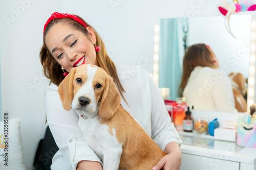 A young woman relaxing and playing with her beagle dog in her makeup dressing table.