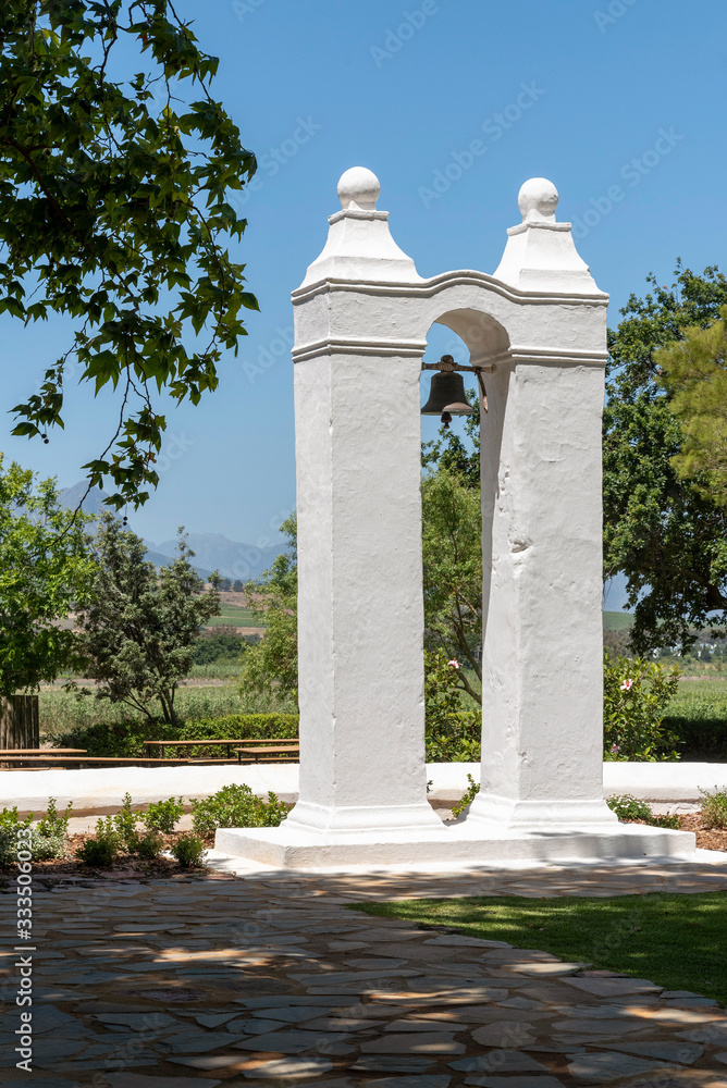 Fototapeta premium Stellenbosch, Western Cape, South Africa. Dec 2019. A slave bell mounted between two white painted pillars on a wine farm in Stellenbosch, Western cape, South Africa.