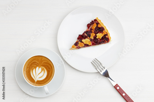 Piece of homemade shortcrust cherry pie and cup of coffee cappuccino on white wooden table. Top view.