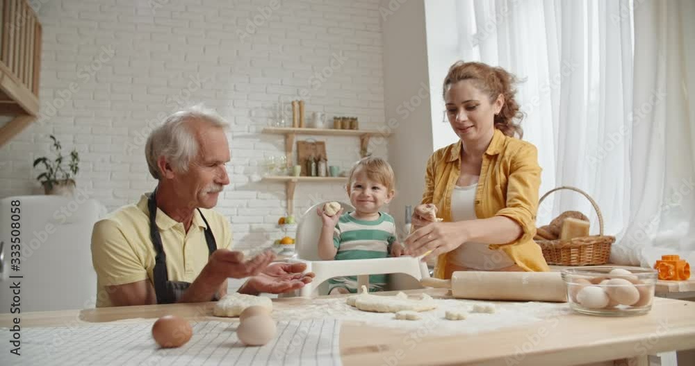 Caucasian family spending time together, dancing while preparing bakery dough. Young mother dancing while little kid and grandfather are happily smiling - family ties concept close up Caucasian family spending time together, dancing while preparing bakery dough. Young mother dancing while little kid and grandfather are happily smiling - family ties concept close up