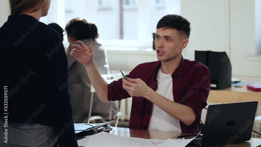 Happy smiling young European male business manager gesturing, talking to female boss at modern office table workplace. Happy smiling young European male business manager gesturing, talking to female boss at modern office table workplace.