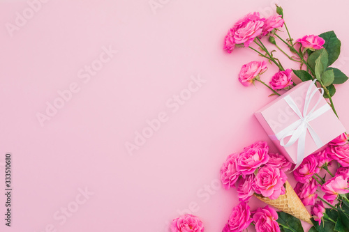 Floral frame of pink roses flowers and gift box on pink background. Flat lay, Top view.