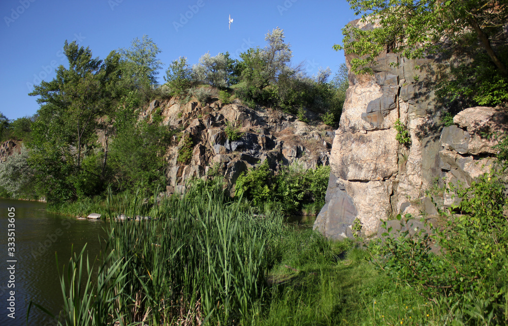 Former stone quarry. Nature Restoration. Summer landscape with river, rocks, green grass, trees and blue sky.