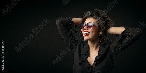 Vivid mischievous young beauty with arms behind head on black isolated background, copyspace
