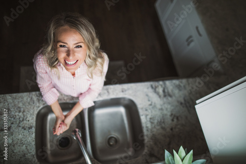 Young woman smiling while washing her hands at the kitchen sink
