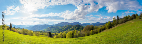 stunning rural landscape in mountains. fields and meadows on hills rolling in to the distant ridge. trees in fresh green foliage. panorama of a countryside on a sunny day in spring. fluffy clouds