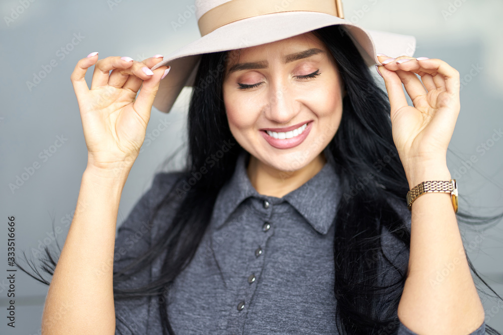 Closeup portrait joyful attractive brunette girl with closed eyes wearing stylish grey dress holding and fashionable hat. Soft focus. Closeup portrait joyful attractive brunette girl with closed eyes wearing stylish grey dress holding and fashionable hat. Soft focus.