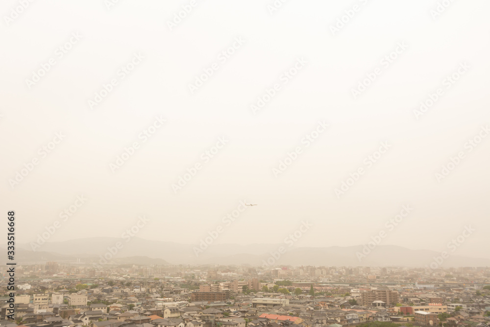 Fototapeta premium 黄砂に覆われた街並みを飛ぶ飛行機
