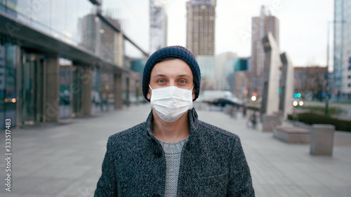 Portrait of Man in Surgical Face Mask Staying Outdside in City Downtown and Looking to Camera. COVID-19 Coronavirus Pandemic Outbreak or Smog Background. Picture with Copy Space photo