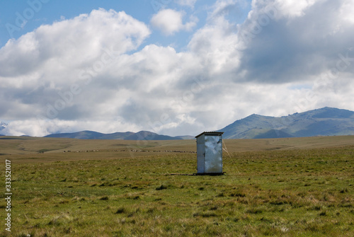 Kyrgyz steppe, near Songkol lake. Metal outhouse in the middle of pasture and mountains in far background. Kyrgyzstan photo