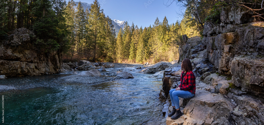 Girl Sitting by the river in the Canadian Mountain Landscape during a sunny winter day. Taken in Golden Ears Provincial Park, near Vancouver, British Columbia, Canada.