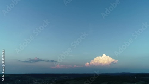 Pink-orange cloud in evening sunrays over blue evening sky with mountains silhouette on the horizon.