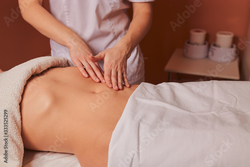The specialist makes the girl a therapeutic massage of the abdomen on the table in the massage parlor.