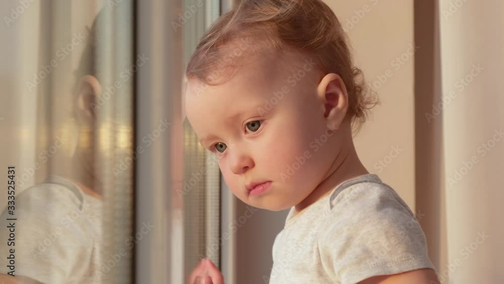 The child looks at the street standing by the window. Slow motion, 4K video. The child looks at the street standing by the window. Slow motion, 4K video.