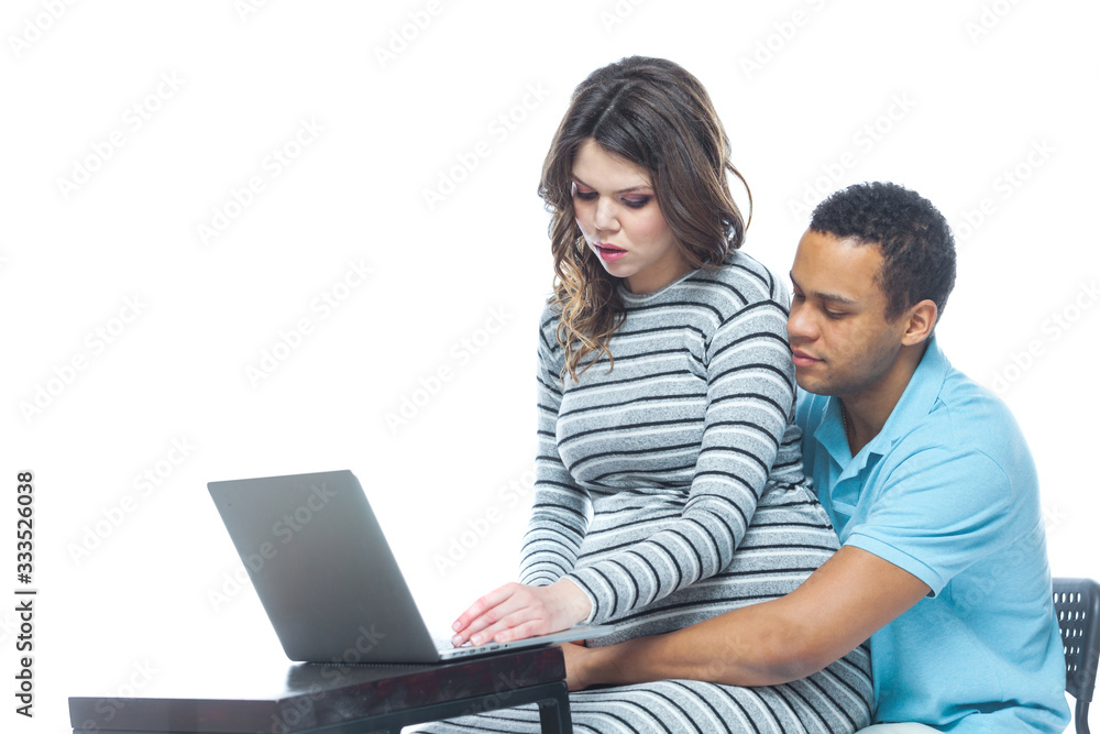 Portrait of a lovely young pregnant couple sitting on a couch with laptop computer. Black man and white woman.
