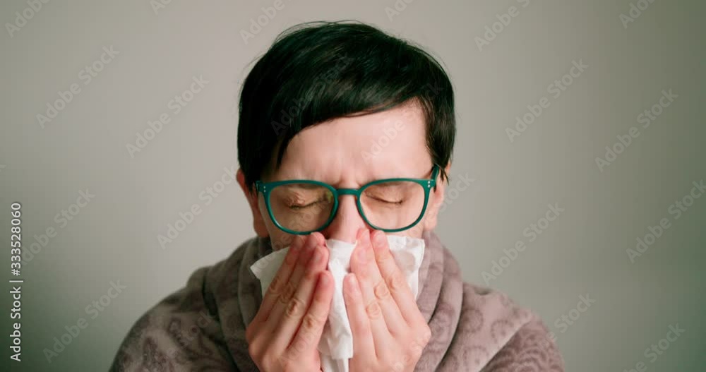 Close up view of Lady with glasses sneezing/ coughing into scarf. isolated on a gray background. Close up view of Lady with glasses sneezing/ coughing into scarf. isolated on a gray background.