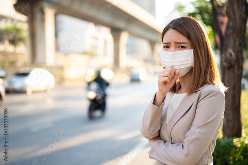 Young business woman wearing surgical mask and coughing while walking in public in Coronavirus or COVID-19 spreading situation