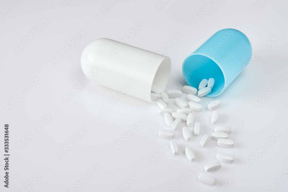 Large open blue with white pill on white acrylic table, with small white pills scattered, close-up shot Large open blue with white pill on white acrylic table, with small white pills scattered, close-up shot