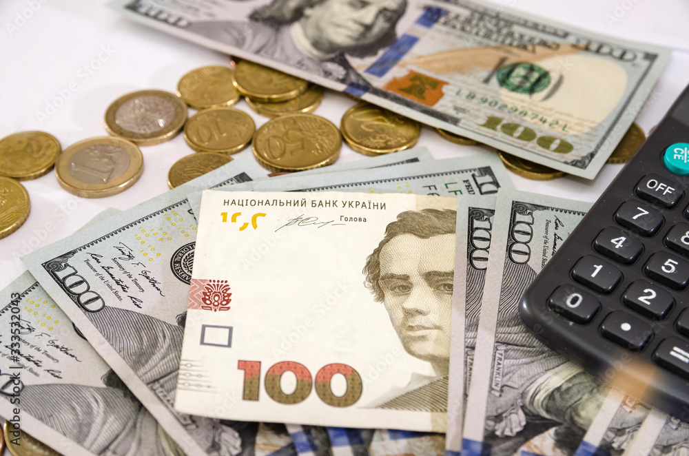 Fototapeta premium 100 hryvnia, coins and part of a calculator among dollars on white. Concept of inflation, financial crisis. Close-up. Money background.