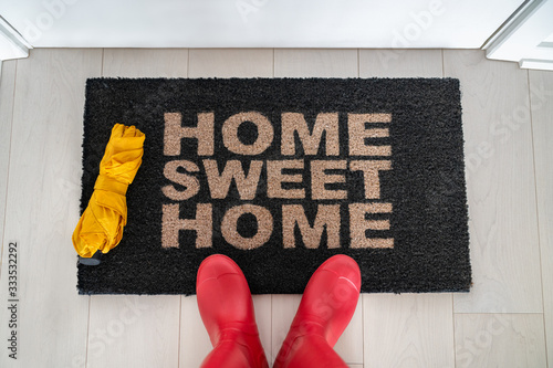 Autumn home sweet home entrance door mat woman taking feet selfie arriving home wiping wet rubber wellington boots and umbrella on rainy day.